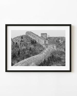 The Great Wall climbs a winter hillside toward a brick watchtower in black and white