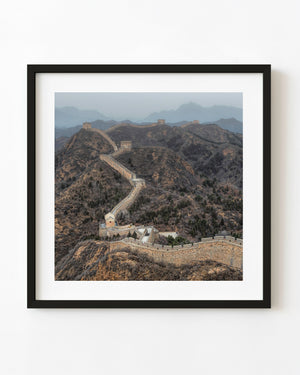 The Great Wall winds across rugged brown hills beneath hazy blue mountain ridges
