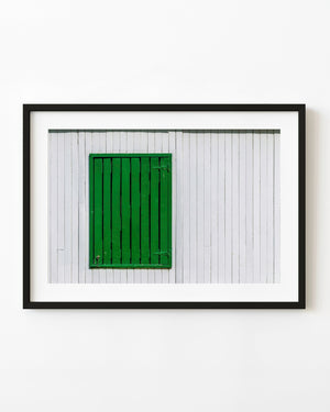 A green wooden shutter contrasts with white vertical wall boards in a colour architecture photograph