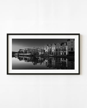 Haarlem canal houses and a moored boat reflect in still water in black and white