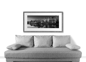 A long moored boat rests beside brick houses reflected on calm Dutch canal water