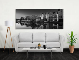 Still canal water doubles the shapes of trees, boats, and gabled urban buildings