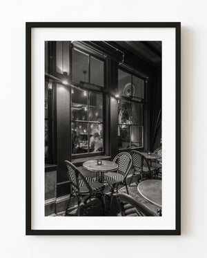 Empty Haarlem café tables and woven chairs stand beside glowing windows in black and white