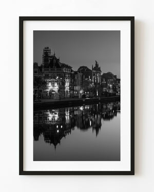 Illuminated Haarlem buildings reflect across the Spaarne in a black and white evening photograph