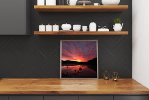 Silhouetted forest borders a quiet lake beneath a vivid crimson sunrise