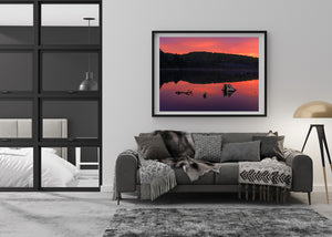 Three tree stumps rise from smooth red and purple morning reflections