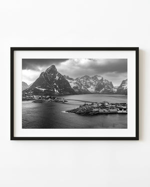 A bridge links Hamnøy waterfront homes beneath snow-streaked Lofoten mountains in black and white