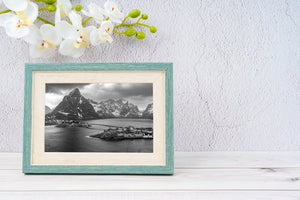 Small houses and wooden cabins stand beside water beneath towering winter peaks