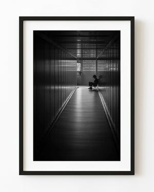 A seated figure appears in silhouette at the end of a Hanoi airport corridor in black and white