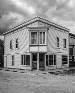 A weathered wooden corner storefront features tall windows and carved double doors