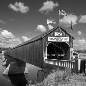 A long wooden covered bridge rests on concrete piers above calm water