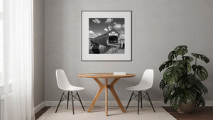 A square monochrome photograph captures the bridge’s wooden siding and river reflections