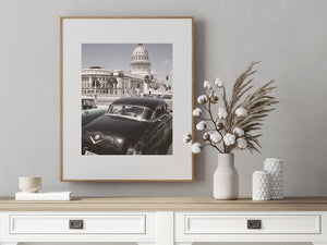 Vintage cars passing Havana’s El Capitolio beneath a pale sky, photographed from street level.
