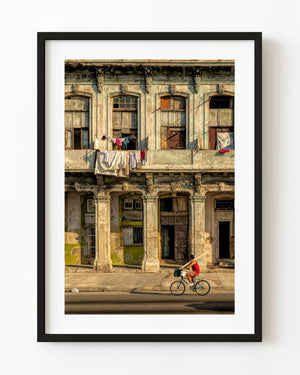 Cyclist passing a weathered Havana building with ornate windows and laundry hanging from a balcony.