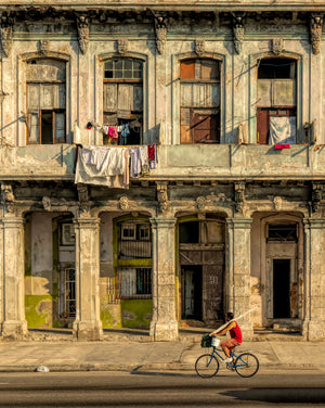 Havana street scene with a blue bicycle beneath a worn facade and sunlit hanging laundry.