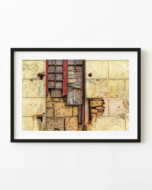 Weathered red window frame and wooden boards surrounded by crumbling yellow plaster in Havana, Cuba.