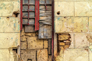 Close-up of a boarded Havana window with peeling red paint and exposed brickwork.