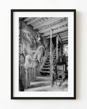 Surreal horse-bird mural beside a worn wooden staircase in a Havana interior, photographed in black and white.