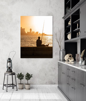 Havana skyline fades into warm light behind a silhouetted fisherman and his fishing rod.