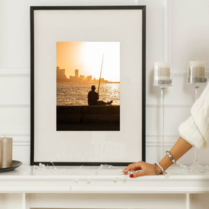 Malecon sunset photograph with a seated fisherman, shimmering water and Havana’s skyline.