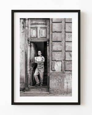 Man carrying a box through a weathered Havana doorway in black and white