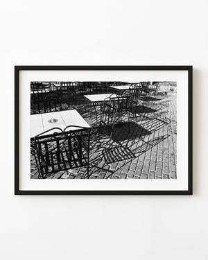 Empty cafe chairs and tables cast patterned shadows across Havana’s Plaza Vieja in black and white.