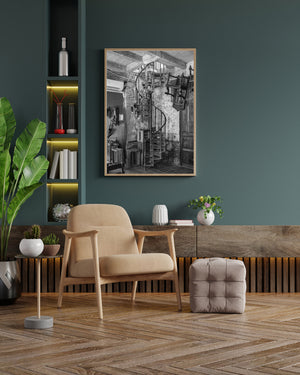 Monochrome interior photograph of an iron spiral stair beside aged plaster and household objects.