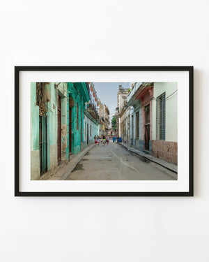People walk along a narrow Havana street between turquoise, pink and weathered pastel facades.
