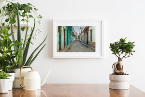 Turquoise doors and pastel walls line a Havana street filled with everyday pedestrian life.