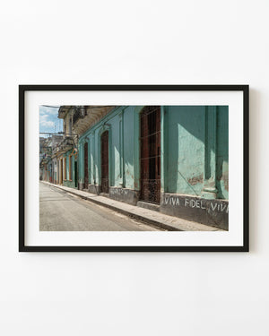 Turquoise Havana facade with tall barred doorways and Viva Fidel graffiti beside a quiet street.