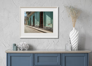 Havana street lined with pastel facades and tall iron-barred doors beside white Viva Fidel lettering.