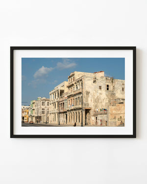 Weathered waterfront buildings in Havana catch warm sunlight beneath a blue sky with scattered clouds.