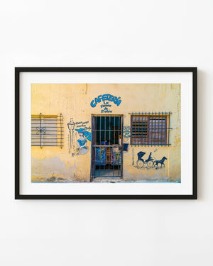 Yellow Havana cafe storefront with blue lettering, barred windows and painted figures around the doorway.