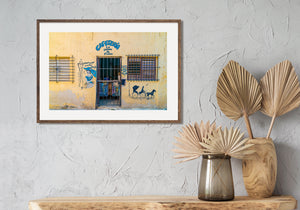 Blue-painted cafe lettering and decorative murals brighten a worn yellow storefront in Havana.