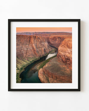 Colorado River winds between red sandstone canyon walls at Horseshoe Bend beneath a warm orange sky.