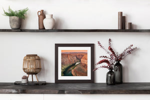 Warm-toned canyon cliffs rise above the Colorado River and green banks at Horseshoe Bend.