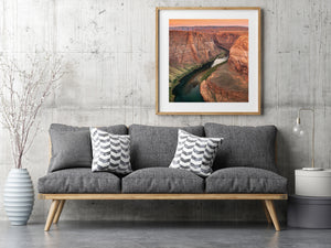 Red sandstone walls frame a winding river beneath an orange sky in a Horseshoe Bend landscape.