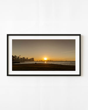 Golden sunrise over the Hudson River and New York skyline, reflected across calm water.