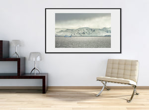Grey water and a pale iceberg beneath broad ice-covered mountains along the Antarctic coast.