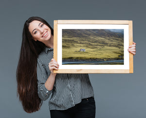An isolated farmhouse stands on a grassy slope beneath fog-covered hills in Iceland.