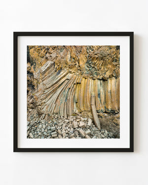 Fan-shaped Icelandic basalt columns with ochre and grey surfaces above scattered broken rock.