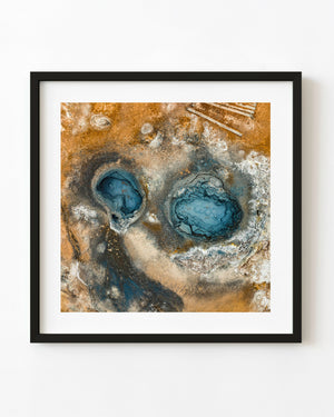 Aerial view of two blue geothermal craters surrounded by ochre earth and pale mineral deposits in Iceland.