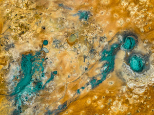 Turquoise geothermal formations and branching channels contrast with ochre earth in an Icelandic aerial landscape.