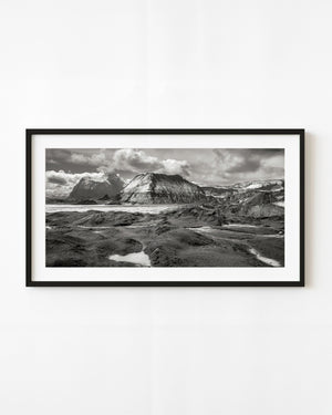 Black and white Icelandic landscape with rugged mountain ridges, shallow pools and a dramatic clouded sky.