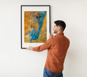 Overhead view of a vivid blue geothermal channel bordered by golden mineral-stained ground.