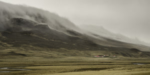 Red roof farm buildings in wide Icelandic valley with misty mountains