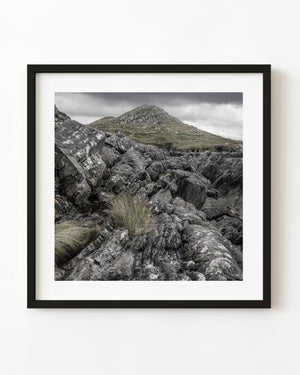 Rugged rock formations and tufts of grass near Inch Beach, Ireland, beneath a grey clouded sky.
