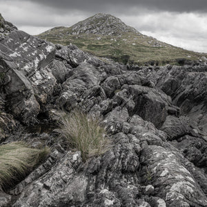 Weathered Irish coastal rocks with pale markings below a grass-covered hill near Inch Beach.