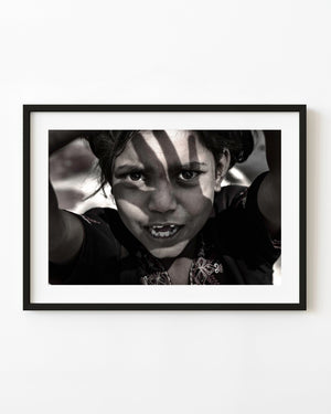 Close sepia portrait of an Indian girl with raised arms and strong shadows across her face.