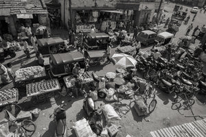 Crowded Indian market street with fruit vendors, auto rickshaws, motorcycles and bicycles seen from above.